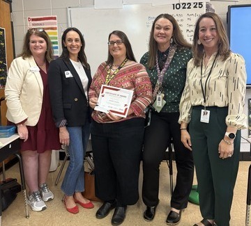 5 women are standing in a classroom. Mrs. Forsythe is in the center, holding a certificate.