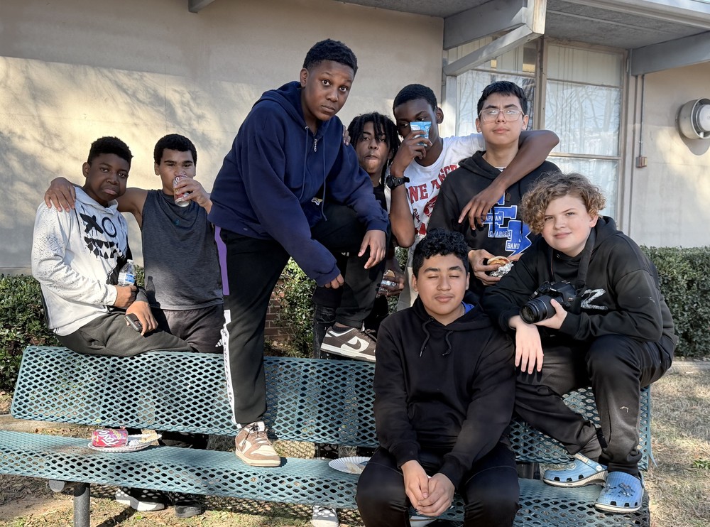 A group of students are gathered together on a bench in the courtyard during the school-wide ACAP & State Report Card celebration.