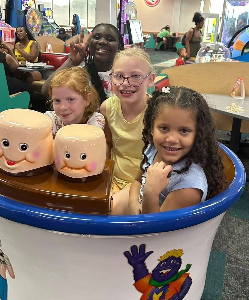 4 young girls are in a teacup ride in the middle of Chuck E Cheese restaurant