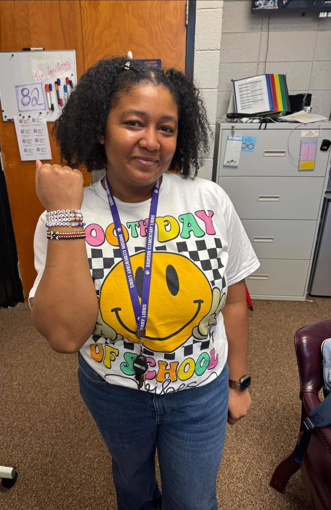 Ms. Langston wears a shirt with a smiley face that says "100th Day of School" while showing her wrist with covered with bracelets.
