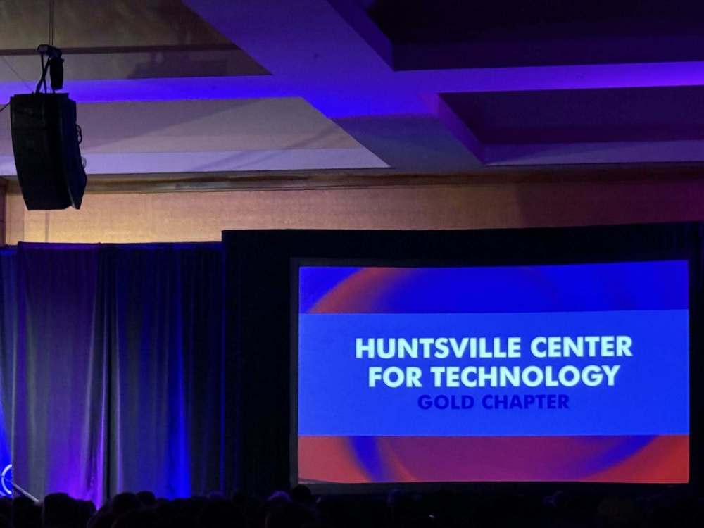 Stage with a projected image on a screen showing Huntsville Center for Technology Gold Chapter