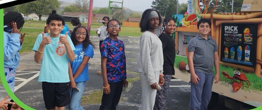 A group of students are standing outside in line at the Kona Ice snowcone truck