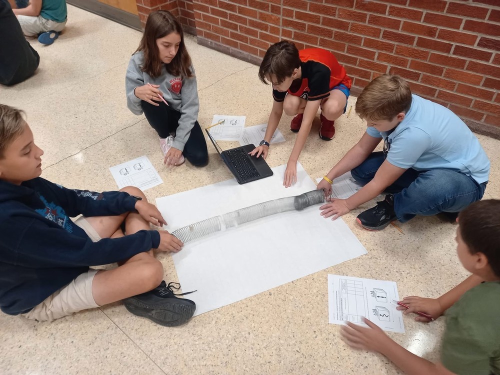 Five 6th grade students are on the floor looking at how a slinky creates a wave