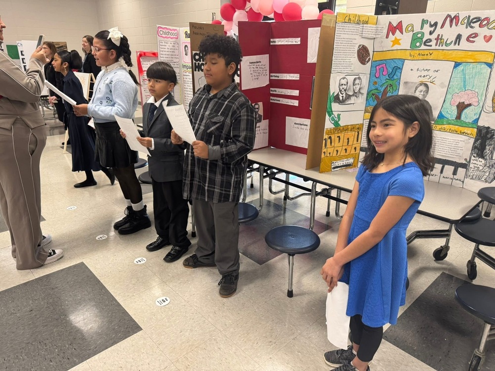 4th grade students in the lunchroom dressed up as their wax museum person. They are standing in front of their board that tells about their person 