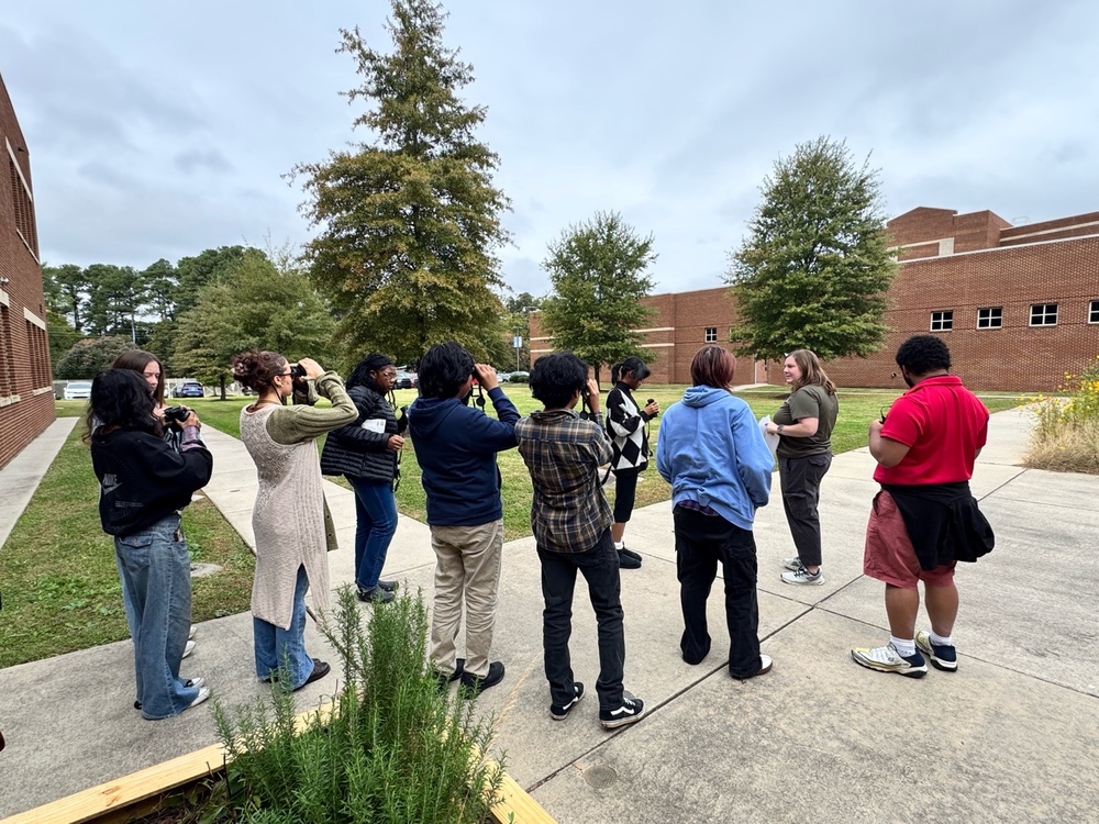 Laura Lambert, Naturalist Educator with the Land Trust of North Alabama, instructs Lee High School Green Ambassadors on binocular use during a bird identification activity in the school courtyard. Students hold binoculars up to their eyes as they practice spotting birds across campus.