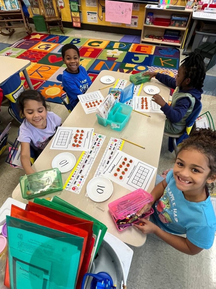 Some students in Mrs. Neighbors sitting at table with pumpkin manipulatives, crayon boxes,  and 10 paper place. 