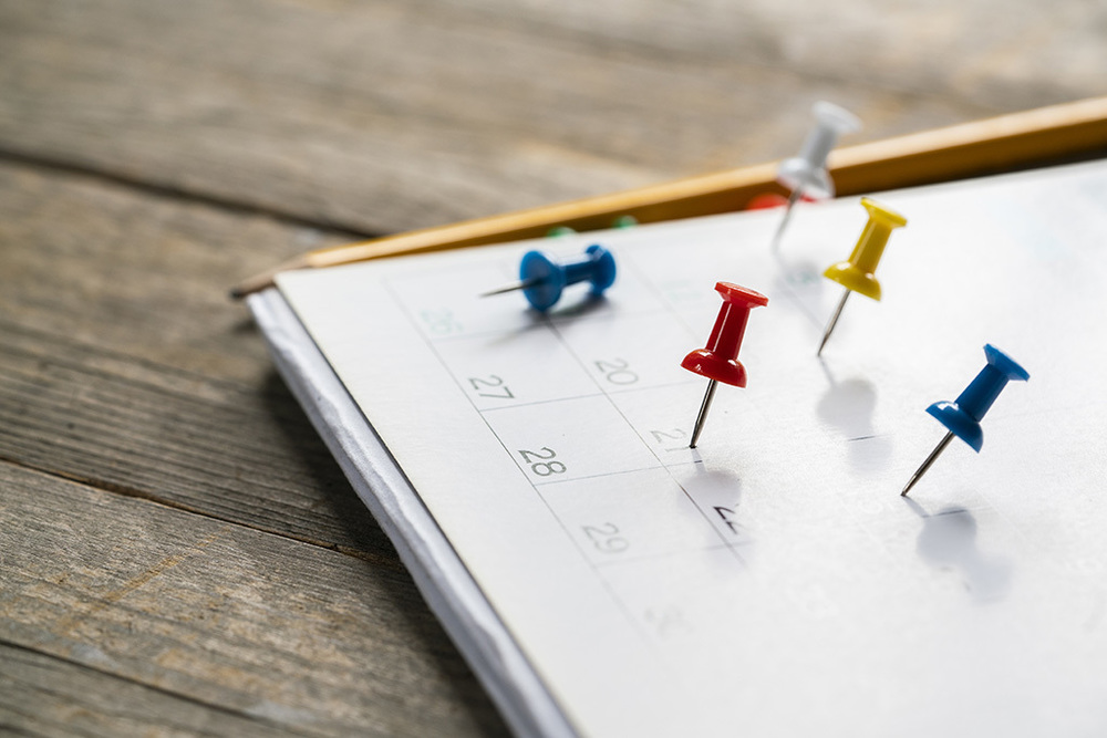 Calendar and pencil on a wooden table with different colored thumb pins stick in various days