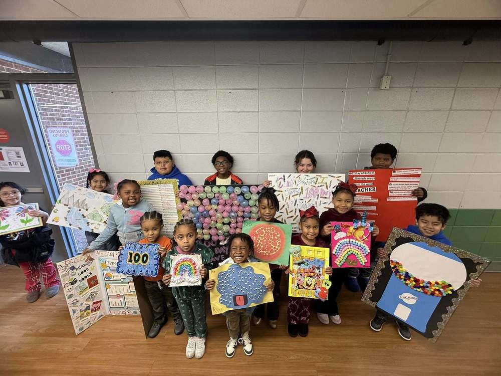 Students smile while holding their 100th Day of School posters