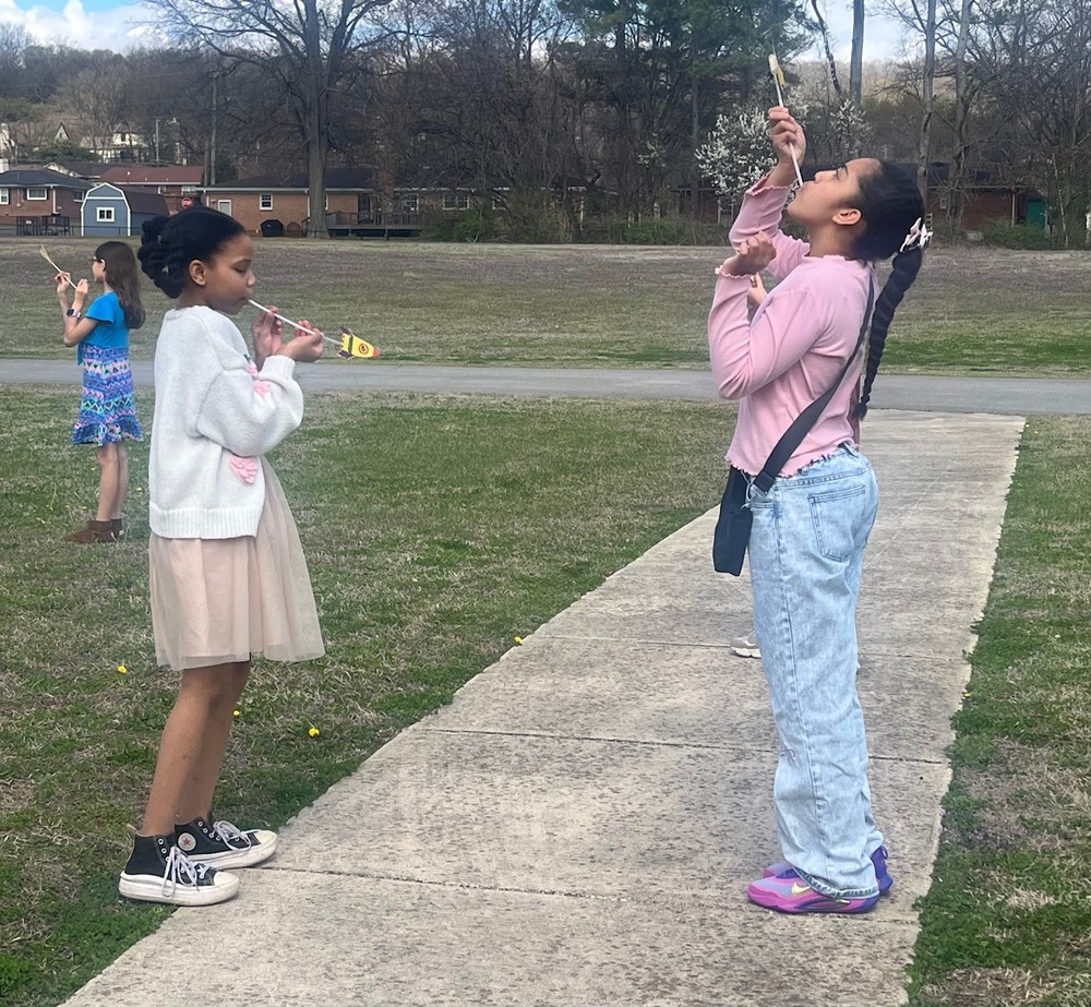 Two female students blow rocket straws for the school's rocket launch party. 