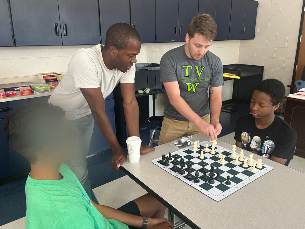 Two teachers show two male students how to play chess.