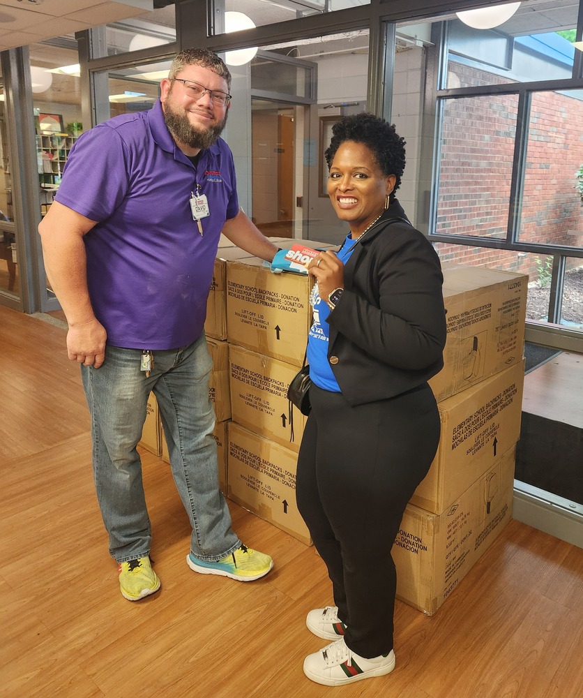 Dr. Headen and a Costco associate smiling while standing in front of a display of 500 donated backpacks.