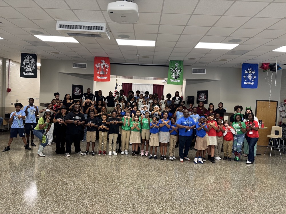 Students, staff, and volunteers standing in front of the stage dressed in house colors; red, blue, red, green