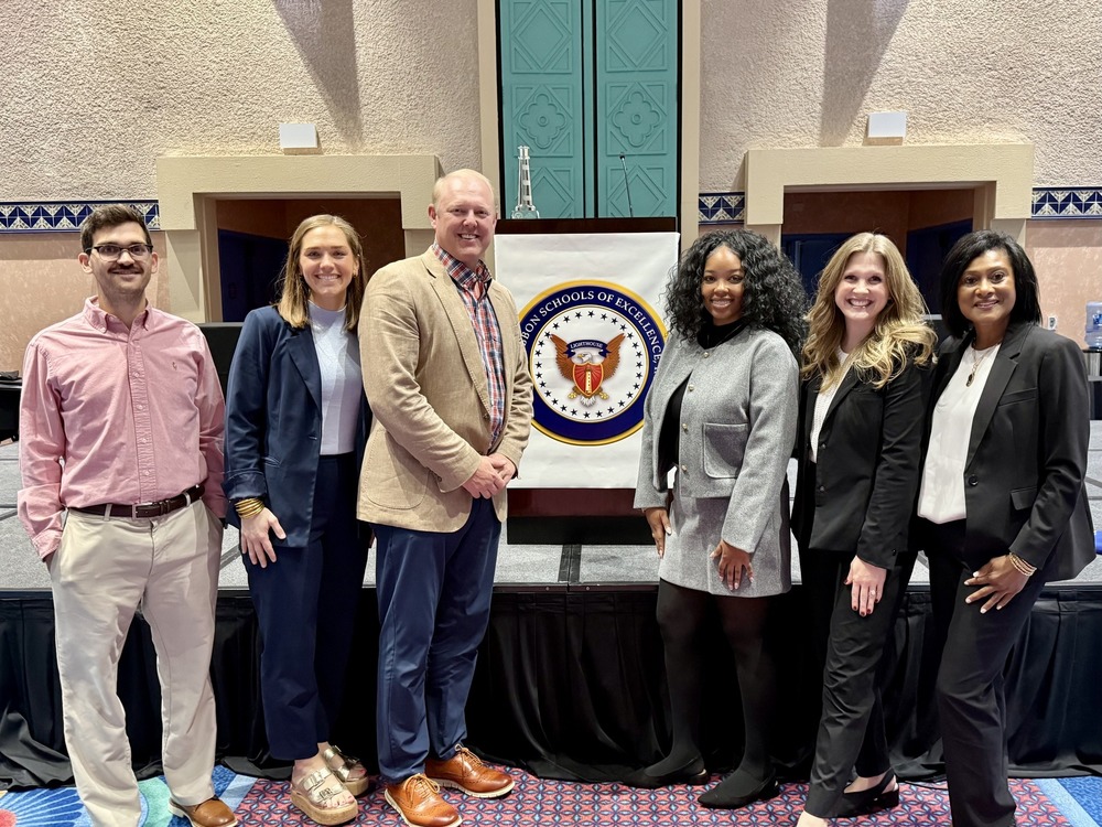 Administrators from AAA Elementary, AAA Middle, Challenger Elementary, Challenger Middle, Grissom High, and Huntsville High post in front of the blue ribbon schools seal