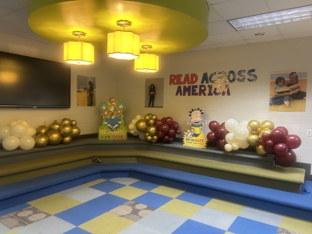 Picture of the RHES library stage with balloons and standing book characters with letters on the wall that say Reqd Across  America