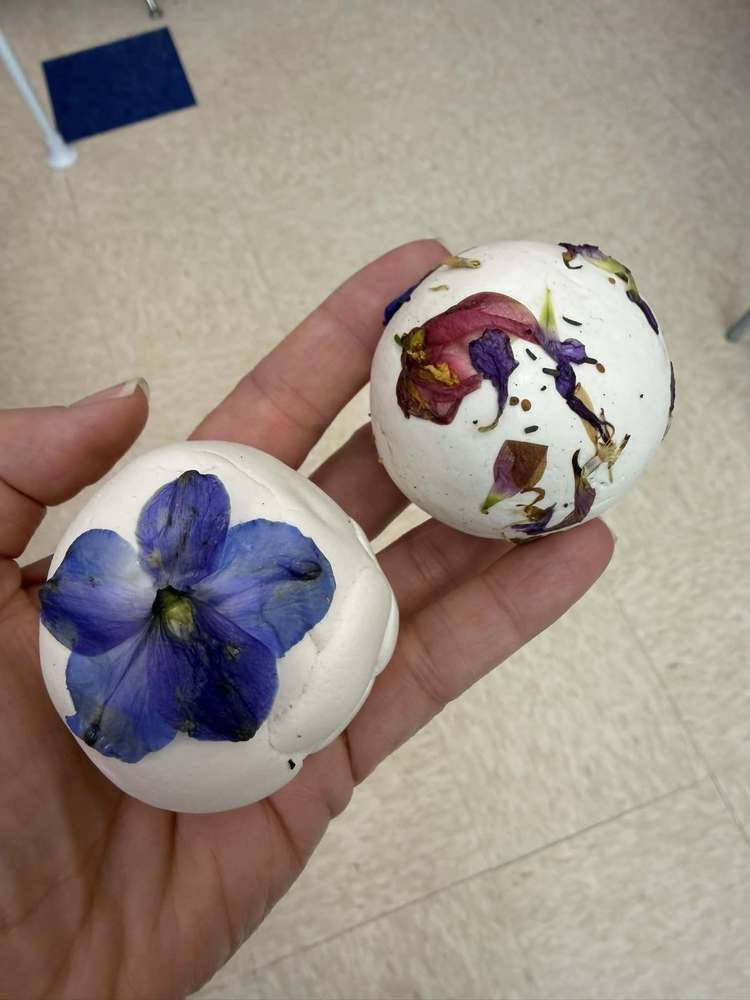 white ball of clay with seeds inside and dry flowers on outside called seed bombs in a hand
