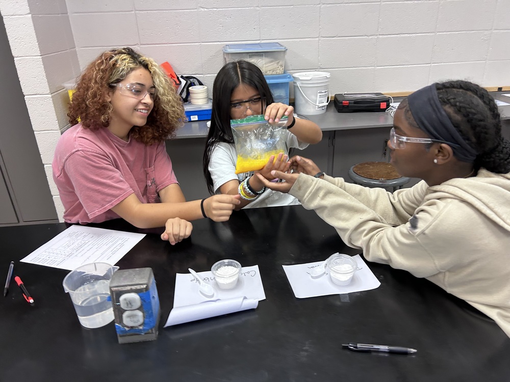three students investigating a chemical reaction in a bag during a science lab