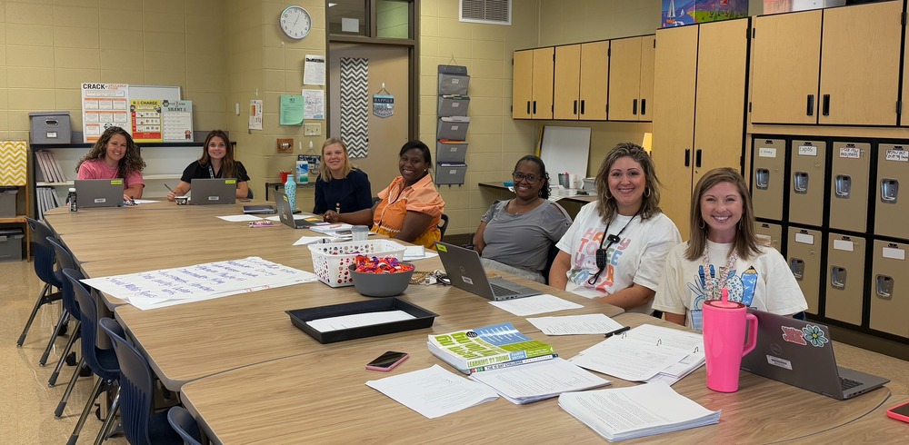 The first grade team of seven teachers sitting at a large table planning instruction for their students.
