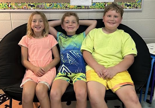 Three Students Sitting in an Oval Char in Neon Clothes in their classroom