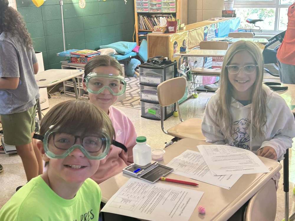 students sitting at table with a lab sheet in front of them while wearing safety goggles