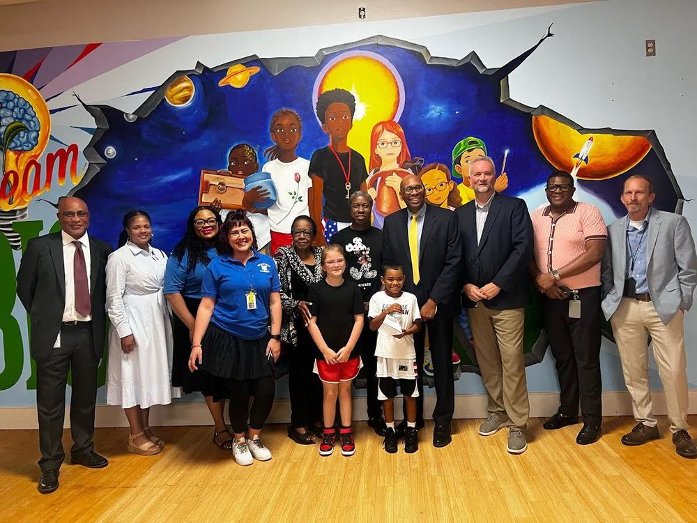 A group of Rolling Hills Elementary staff, students, and community guests stand together in front of a newly unveiled mural by artist John “Jahni” Moore. The colorful mural features children, planets, and vibrant imagery representing learning, creativity, and imagination.
