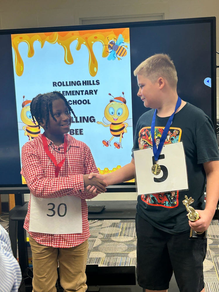 The top two spelling bee contestants shake hands, smiling at each other in a moment of sportsmanship