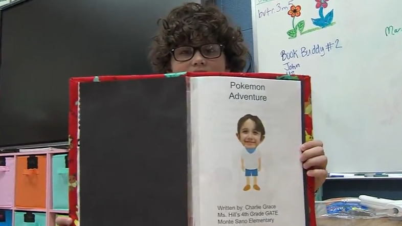Student holding handmade book with Pokemon Adventure titled and picture of student head with clipart body