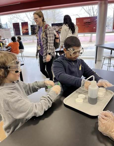 Students sit together wearing safety goggles as they carefully mix materials to create rocket fuel during a hands-on science activity