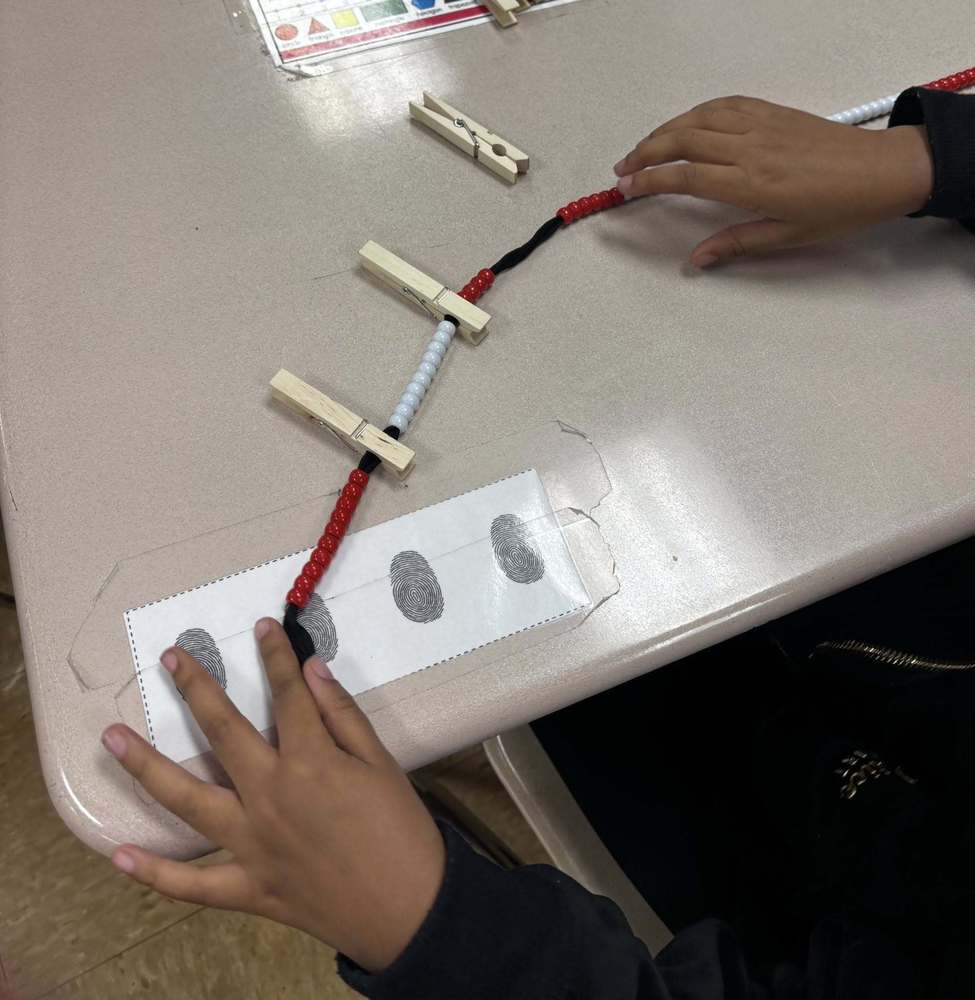 A string nof red and white beads are on a desk with two clothespins clipped on it.