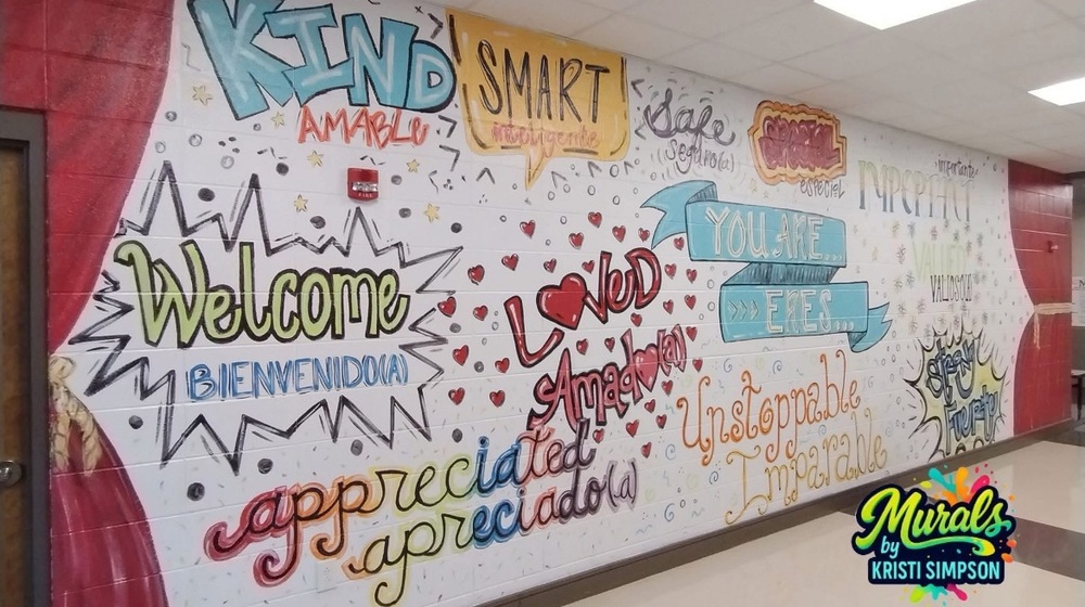 A mural on the wall that was commissioned by the Morris Elementary principal to inspire the students with the words Welcome, loved, unstoppable and kind to name a few. The words are in English and Spanish.
