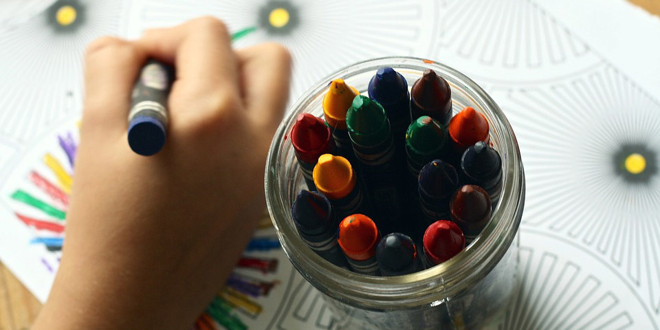 Child's hand coloring next to a jar of crayons
