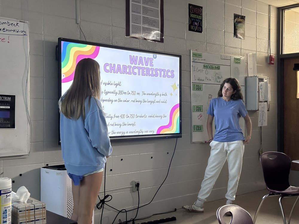 two students standing in front of the smart board presenting their wave project