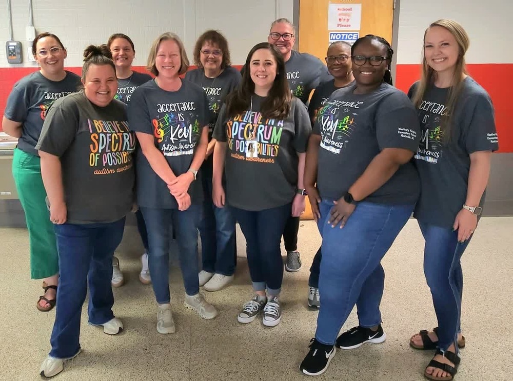 WHES teachers in autism awareness t-shirts gather in a hallway, promoting inclusivity and support.