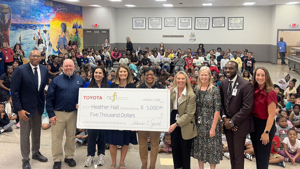 Heather Hall holding giant $5,000 check alongside Dr. Sutton, Toyota reps, other HCS leadership, and standing in front of students at Montview