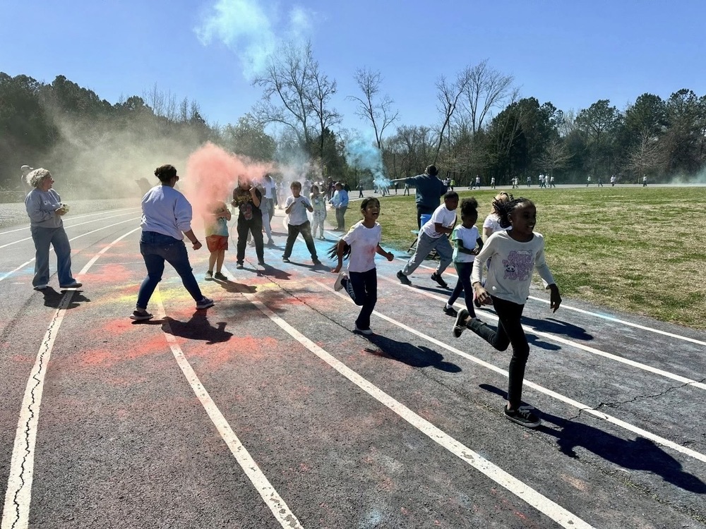 Students and teachers running around the track as color is thrown on them.