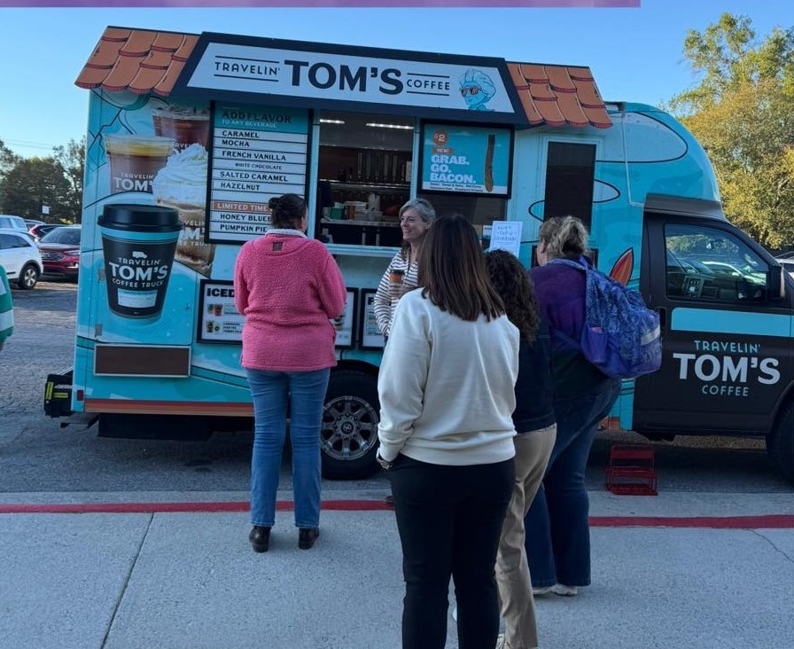 Travelin' Tom's Coffee truck with a group of women waiting in line. The truck is blue with pictures of coffee drinks on the side.