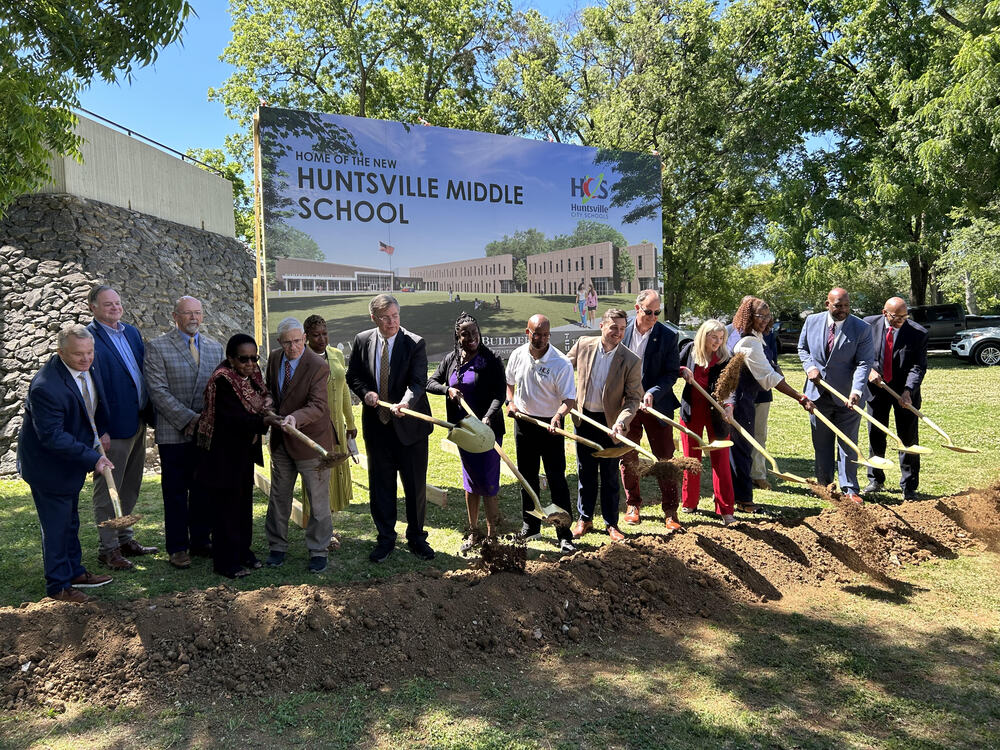 District and school staff break ground with shovels at the new Huntsville Middle site, in front of the artist's rendering.