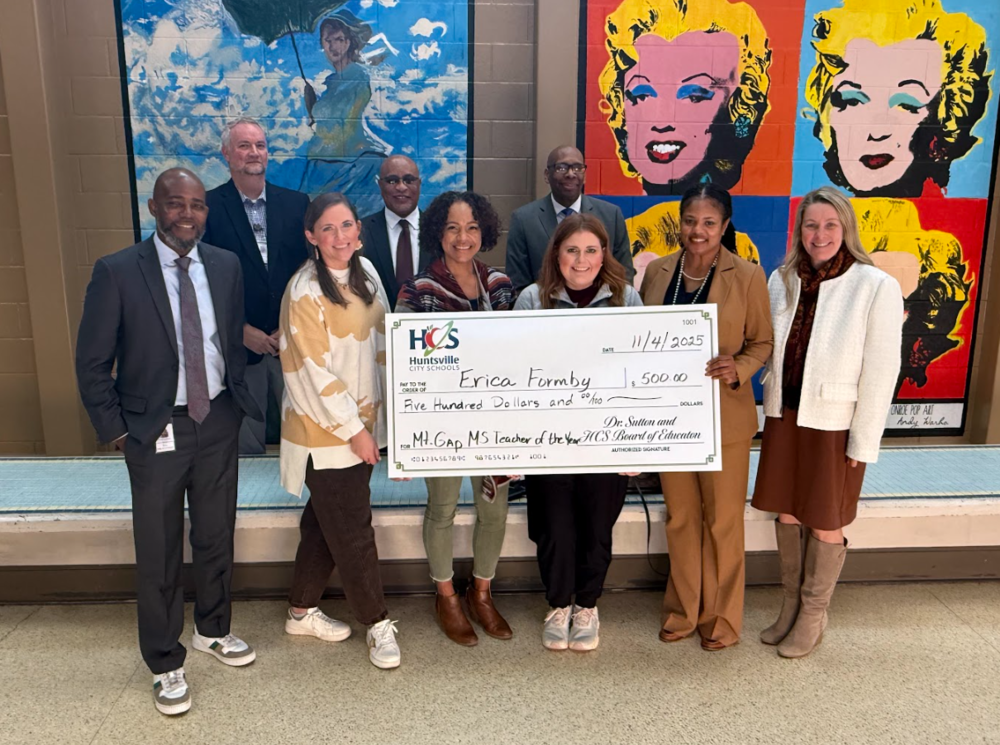 A group of people from Huntsville City Schools surrounding Mrs. Formby in the middle behind a check that was presented to her for teacher of the year