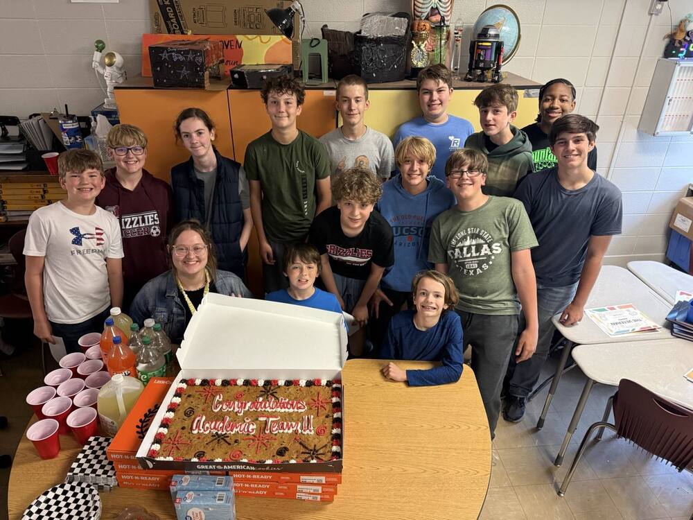 Academic Team taking a group picture with a cookie cake in front of them on a table