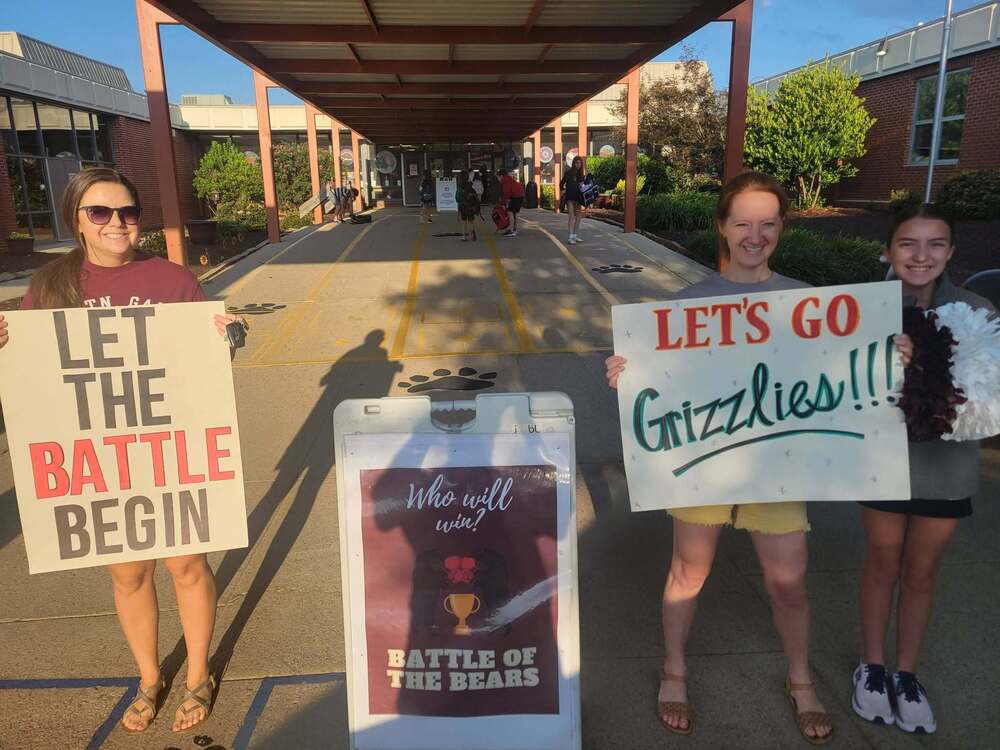Middle school students and PTA member stand outside MGMS holding signs to advertise PTA's Battle of the Bear's fundraiser