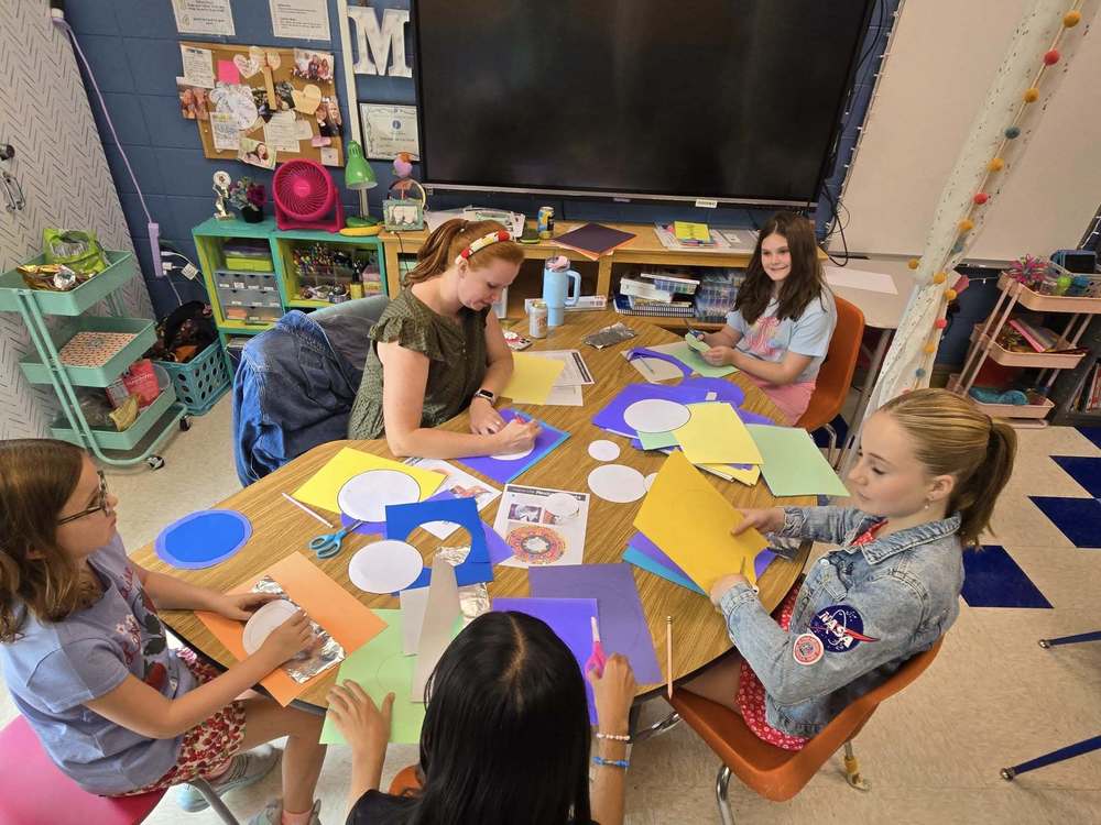 students sitting at table surrounded by art supplies