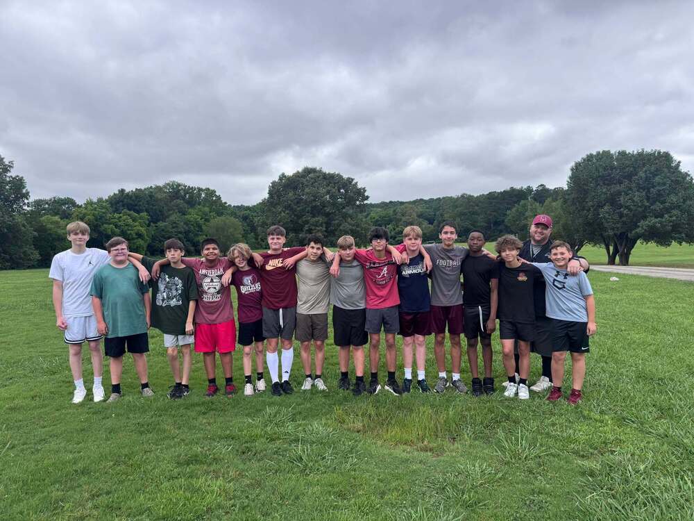 a group picture of the football team standing on a grass field. There are trees behind them and a gray sky above. 