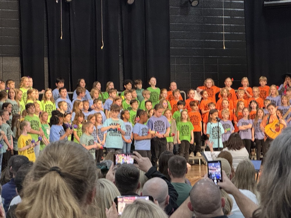 Students is various colored shirts are singing on stage in the GSES cafeteria