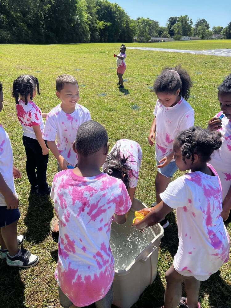 Students smiling and laughing while participating in a water game during Field Day activities outdoors