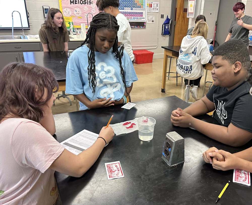 three students at the lab table writing their observation about the fortune teller fish