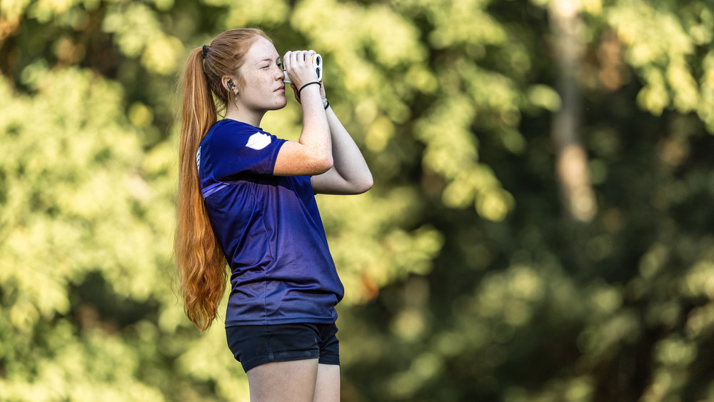 Female student looks through range finder on the disc golf course.