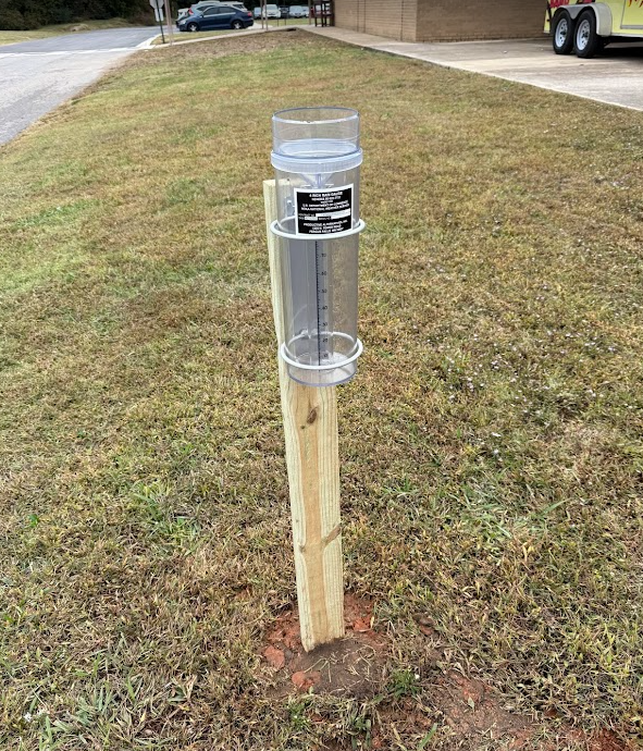 4x4 post in the ground with clear cylindrical container used to collect and measure precipitation