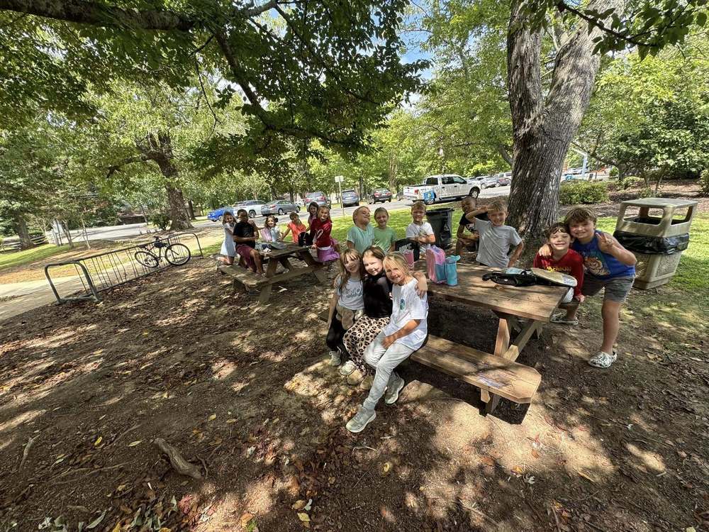 Students sitting outside on wood table enjoying a picnic under a tree