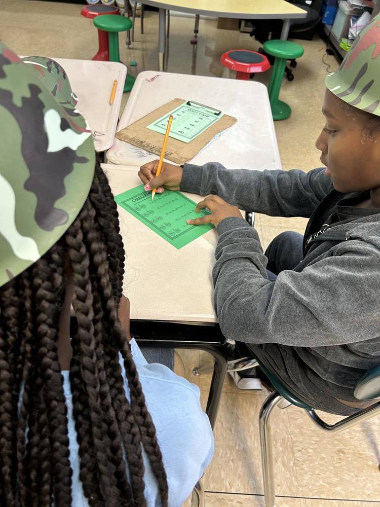 2 students are working at a desk on math, wearing military hats