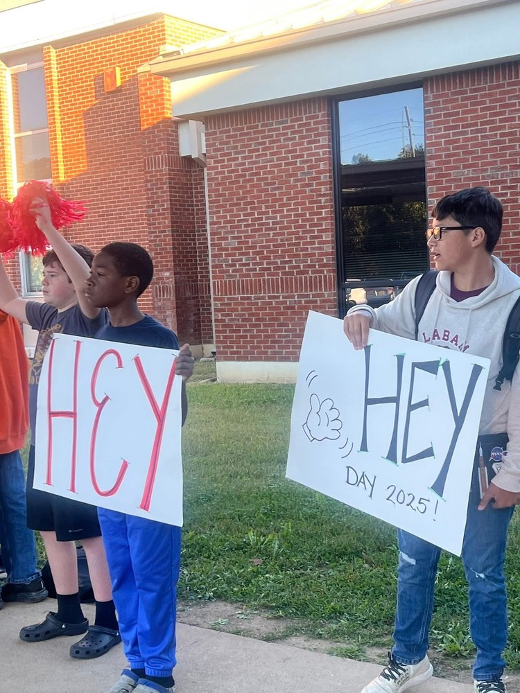 students holding signs that say "hey" to greet other students in the morning
