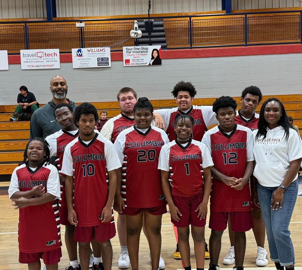 9 adaptive basketball team players standing with coaches wearing their red, black and white uniforms standing in gym posing for picture